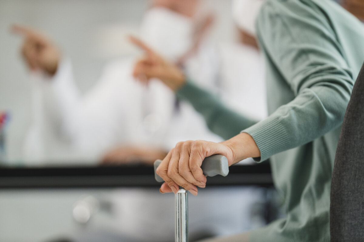 A caregiver steadying an older person’s hand on a walking cane