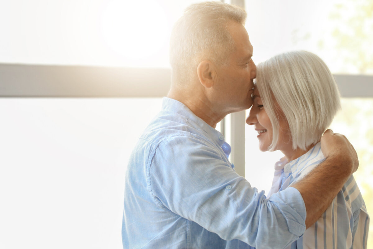 An older couple embracing quietly in a sunlit room at home