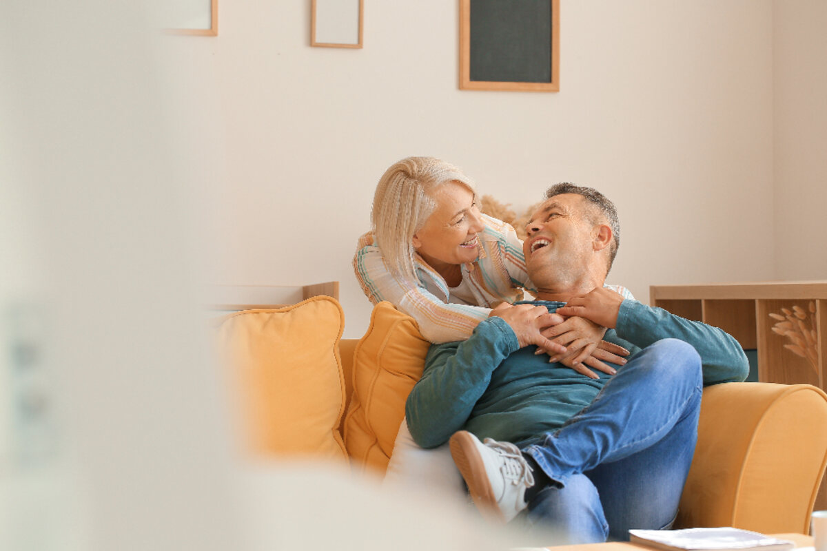 An older couple laughing together at home on the sofa