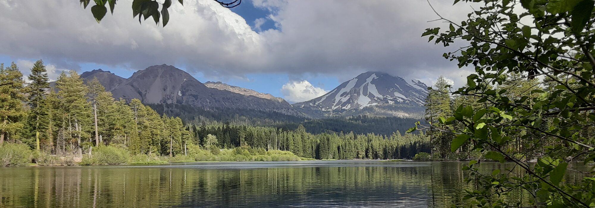 A still mountain lake reflecting snow-capped peaks and pine forest